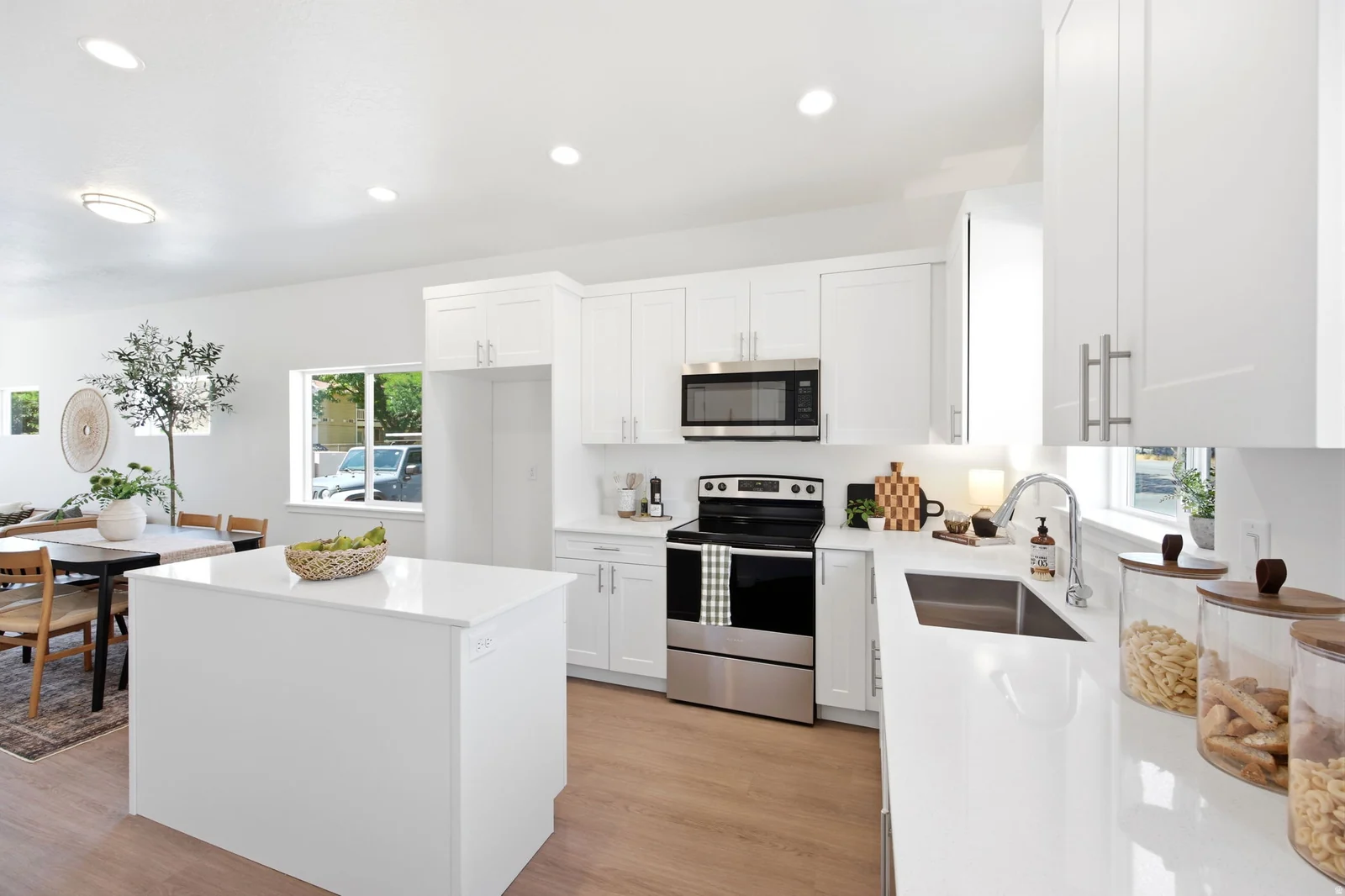 Kitchen featuring white shaker cabinetry, stainless steel appliances, a white island with countertop, and wood-finish flooring